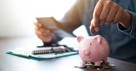 Een mannenhand die munten in een roze spaarpot stopt om geld te sparen